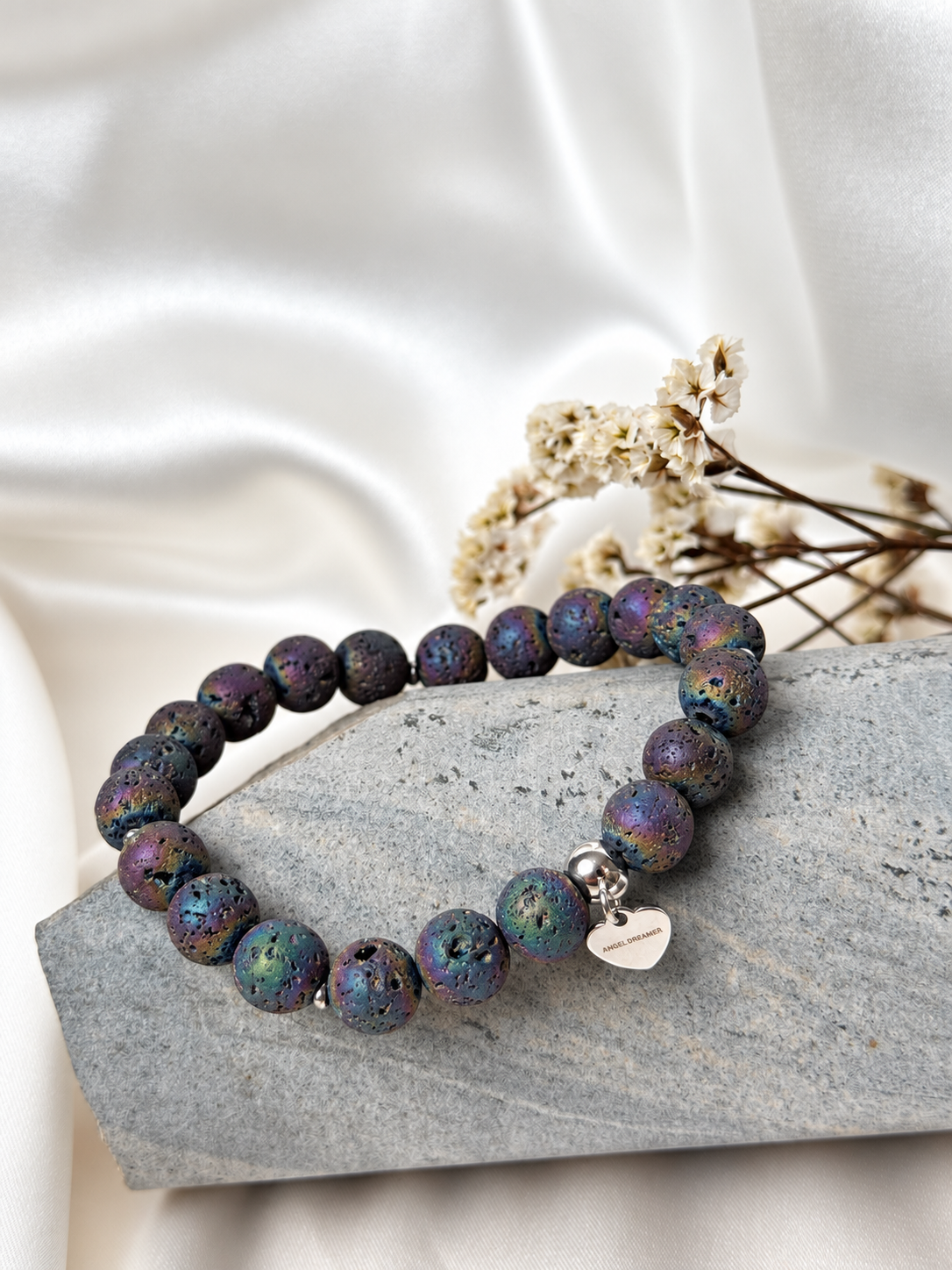 A handmade bracelet featuring textured lava stone with an iridescent finish in purple, blue and green tones. Silver-tone accents and a delicate heart charm complete this distinctive design, perfect worn alone or stacked with other bracelets.

Stone size: 8 mm
Bracelet size: approximately 17 cm
