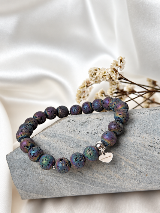 A handmade bracelet featuring textured lava stone with an iridescent finish in purple, blue and green tones. Silver-tone accents and a delicate heart charm complete this distinctive design, perfect worn alone or stacked with other bracelets.

Stone size: 8 mm
Bracelet size: approximately 17 cm