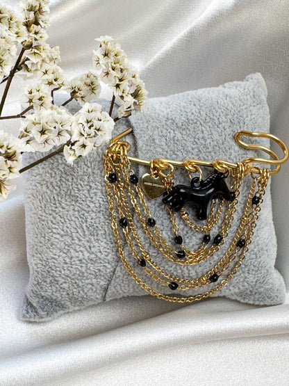 A handmade statement brooch featuring a glossy black horse charm, layered gold-tone chains and small black beads. Its compact 5 × 5 cm size makes it easy to pin to a blazer, coat or bag for a distinctive finishing touch