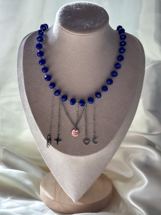 A handmade necklace featuring vivid blue faceted beads, silver-tone chains and a playful mix of dangling charms. The necklace measures 47 cm, with a 6 cm extension chain that allows it to be worn at lengths up to 53 cm. The clasp can also be fastened along the chain for a shorter fit.