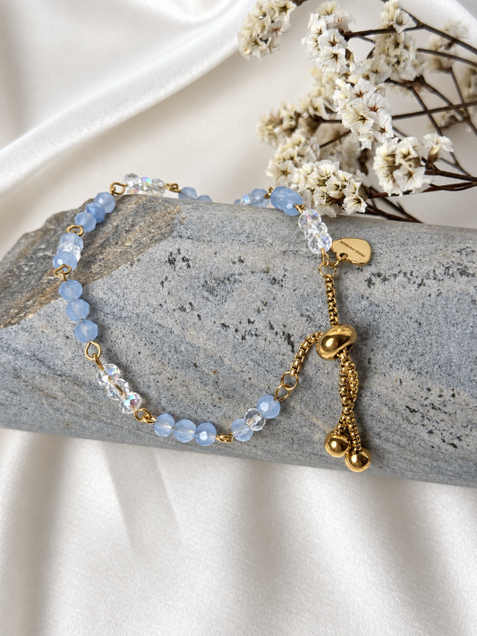 A handmade bracelet featuring soft blue and iridescent clear glass crystal beads, linked with gold-tone details and finished with a delicate heart charm. A light, elegant design, perfect worn alone or layered with other bracelets.

Bead size: 4 mm
Bracelet length: approximately 17 cm + 3.5 cm extension chain