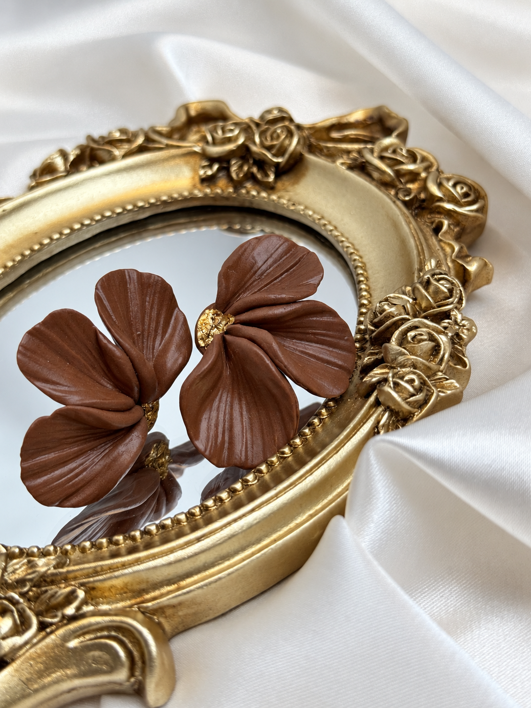 Handcrafted polymer clay earrings featuring softly sculpted petals in a warm cocoa-brown shade. Delicate folds, a gentle sheen and gold-tone centres create an elegant, nature-inspired design. A beautiful finishing touch for neutral outfits, cosy knitwear or a special occasion.

• Material: Polymer clay
• Colour: Cocoa brown with gold-tone accents
• Size: Approximately 4 cm

Each pair is shaped and decorated by hand, so slight variations in texture and form make every pair unique.