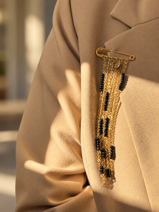 A handmade statement brooch featuring cascading A gold-tone chains and black beads. The longest chain measures 16 cm, and the brooch pin measures 5 cm. Pin it to a blazer, coat or dress for an elegant finishing touch.