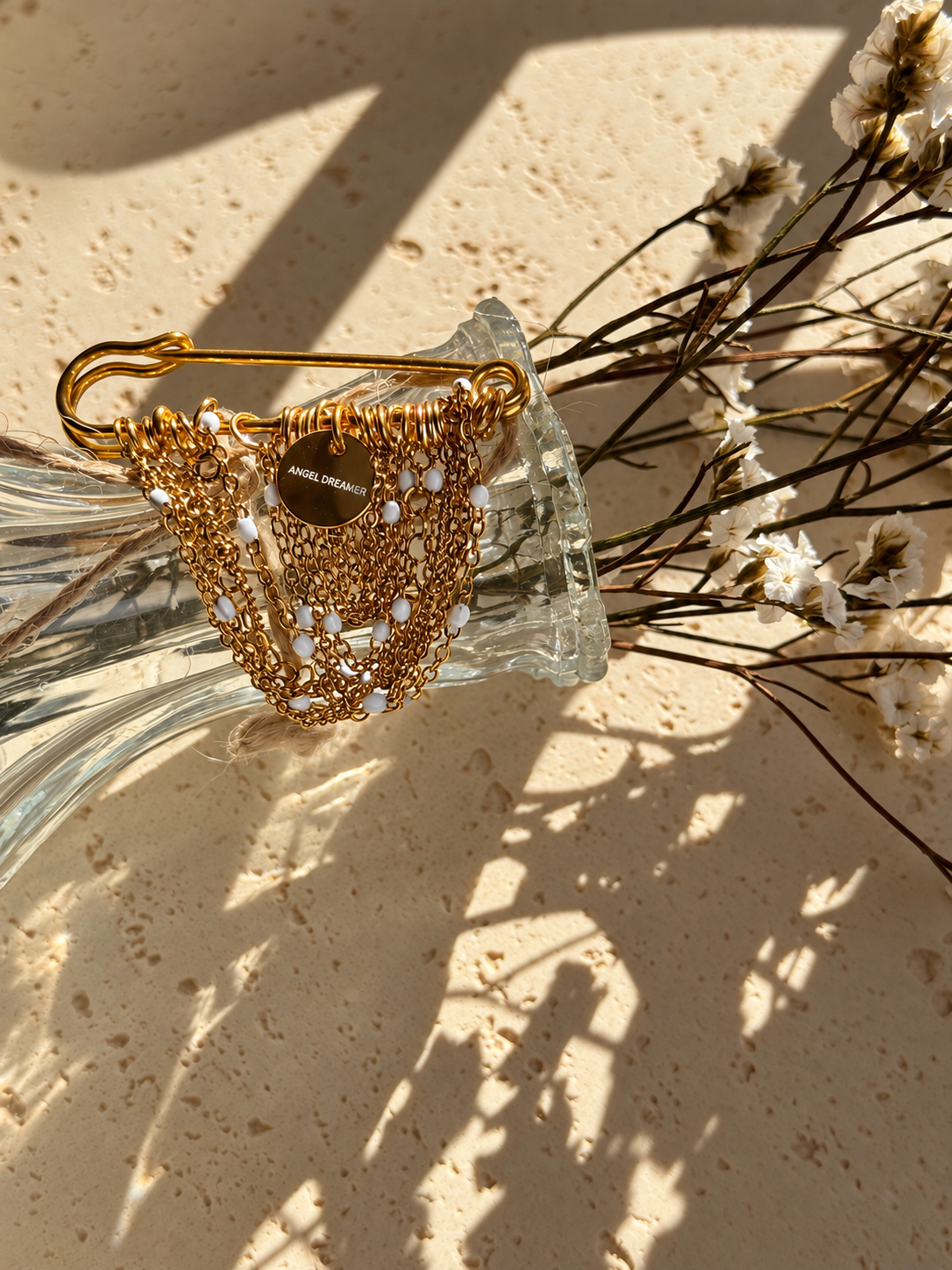 A handmade brooch with layered gold-tone chains, small white beads and an Angel Dreamer charm. The draped chains give it a soft, elegant look. Pin it to a blazer, coat or dress for a distinctive finishing touch.
The brooch measures approximately 5 × 5 cm.