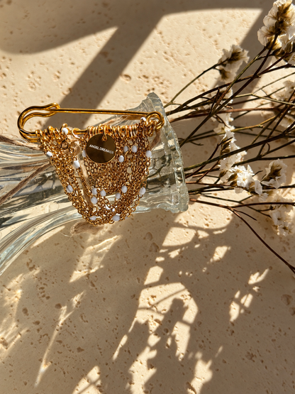 A handmade brooch with layered gold-tone chains, small white beads and an Angel Dreamer charm. The draped chains give it a soft, elegant look. Pin it to a blazer, coat or dress for a distinctive finishing touch.
The brooch measures approximately 5 × 5 cm.