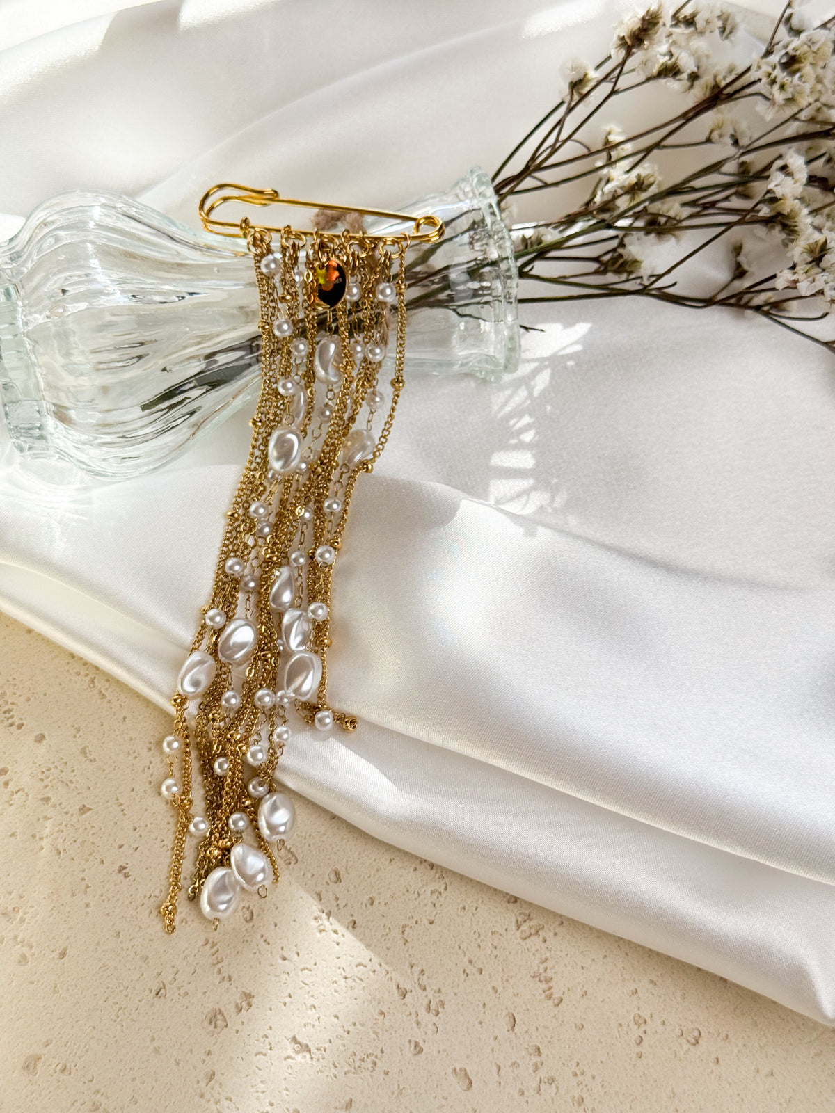 Add an elegant finishing touch with this cascading chain brooch. Delicate gold-tone chains and white pearl-like beads create movement and texture, whether pinned to a blazer, coat or dress.

The brooch measures 5 cm across, and the longest dangling chain measures approximately 16 cm.
