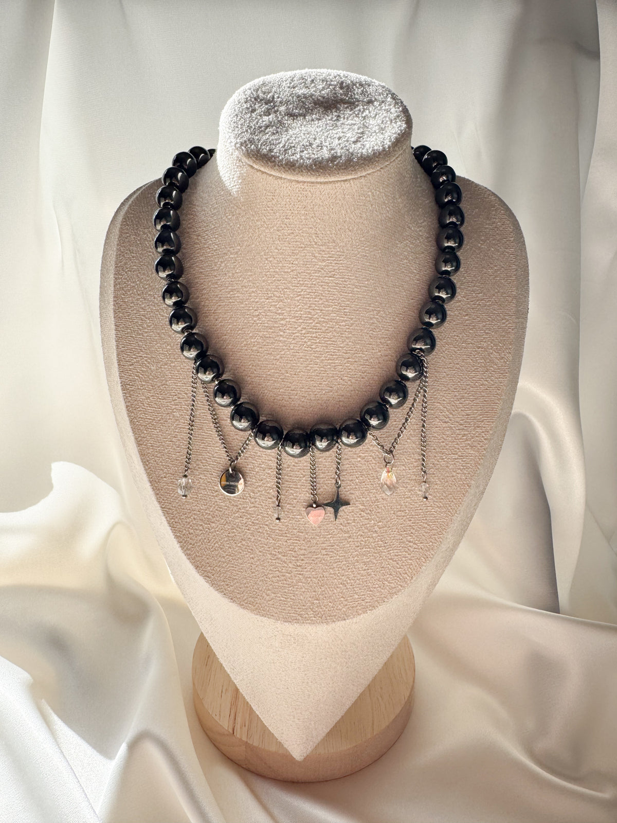 Hematite bead necklace with dangling silver-tone chains and charms, displayed on a jewelry bust.