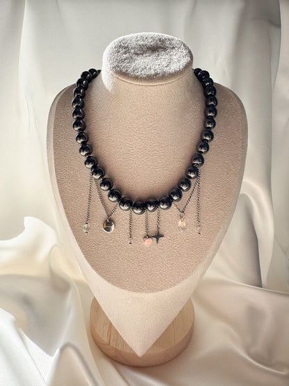 Hematite bead necklace with dangling silver-tone chains and charms, displayed on a jewelry bust.