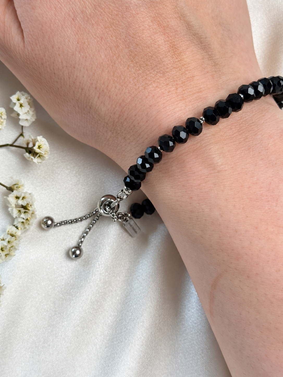 An elegant handmade bracelet featuring black faceted beads and delicate silver-tone spacers. The beads catch the light with a subtle sparkle, making this classic design a beautiful accessory for everyday wear or special occasions.

Finished with an adjustable sliding clasp and two chain ends tipped with silver-tone beads.

Length: Approximately 18 cm, with approximately 3 cm of additional chain adjustment.