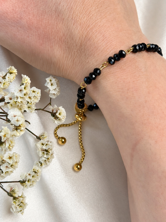 An elegant handmade bracelet featuring black faceted beads arranged in groups of three and joined by gold-tone links. The contrast of deep black and warm gold adds a timeless touch, while the beads catch the light with a subtle sparkle. Beautiful worn alone or layered with other bracelets.

Finished with an adjustable sliding clasp and two delicate chain ends with gold-tone beads.

Size: Approximately 18 cm, with around 3 cm of additional adjustment, allowing a fit of approximately 18–21 cm.
