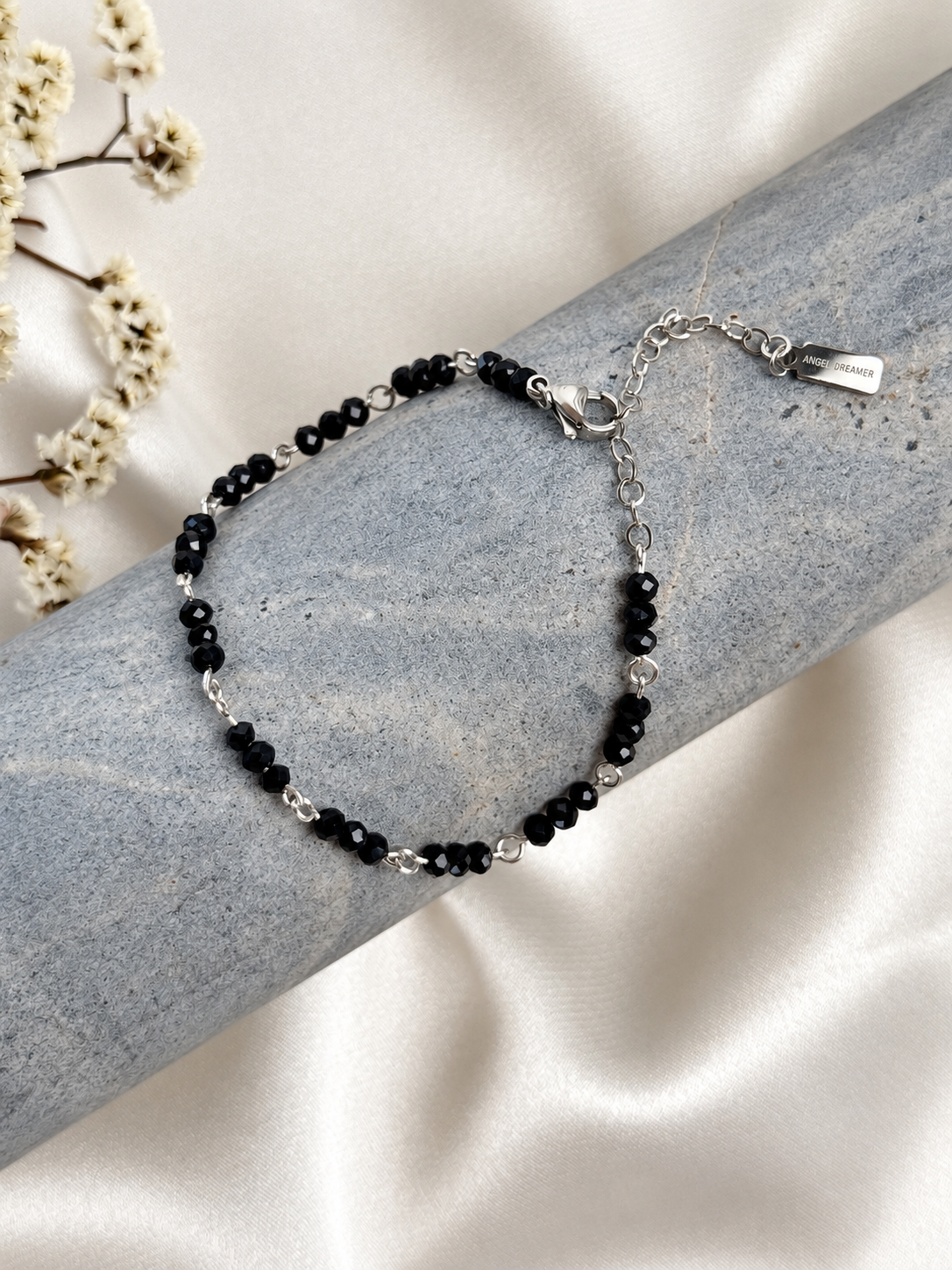 A delicate handmade bracelet featuring black faceted beads arranged in groups of three and joined by silver-tone links. The beads catch the light with a subtle sparkle, while the classic black and silver-tone combination complements both everyday outfits and evening looks. Beautiful worn alone or layered with other bracelets.

Length: 18 cm + 5 cm extension chain, adjustable from 18 to 23 cm. Finished with a lobster clasp.