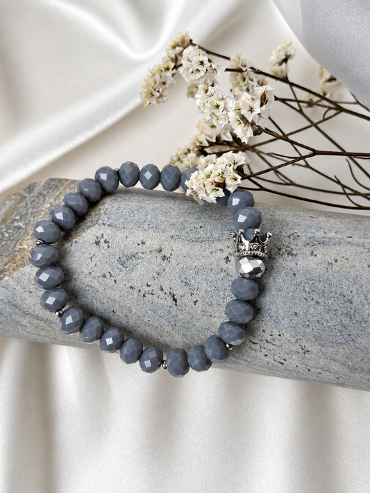 A handmade bracelet featuring faceted glass crystal beads in soft grey tones, complemented by silver-tone accents and a decorative crown. An elegant design with a subtle sparkle, perfect worn alone or stacked with other bracelets.

Bead size: 8 mm
Bracelet size: approximately 18 cm